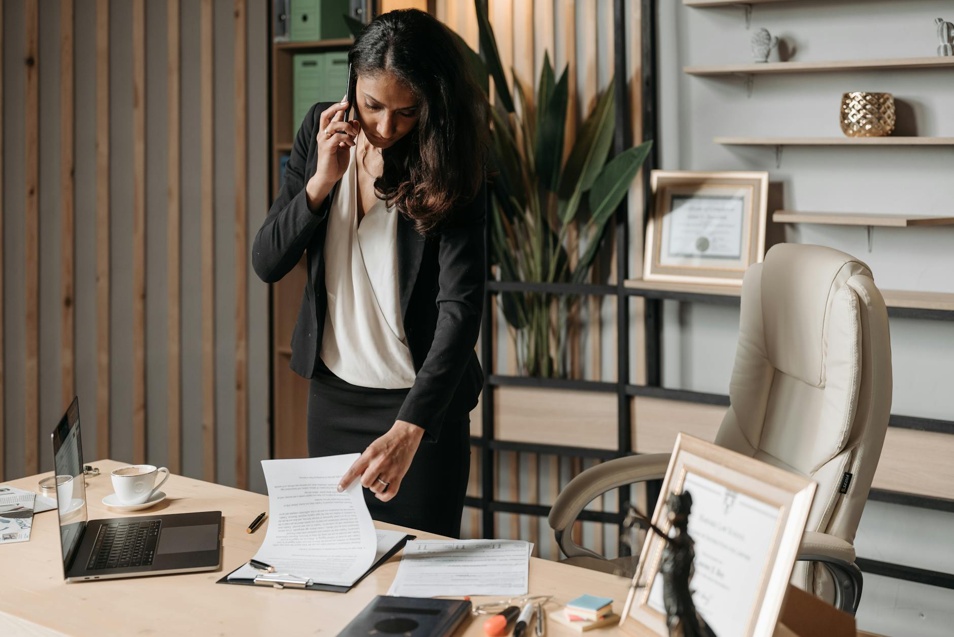 A female lawyer talking on phone while reviewing legal documents in a modern office setting.