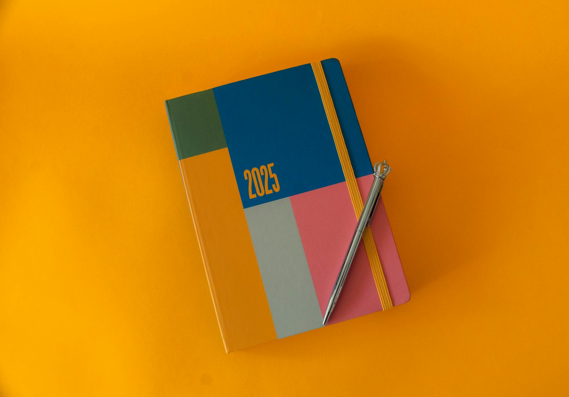 A vibrant 2025 planner with elegant pen on a bold yellow surface, perfect for organizing the year.