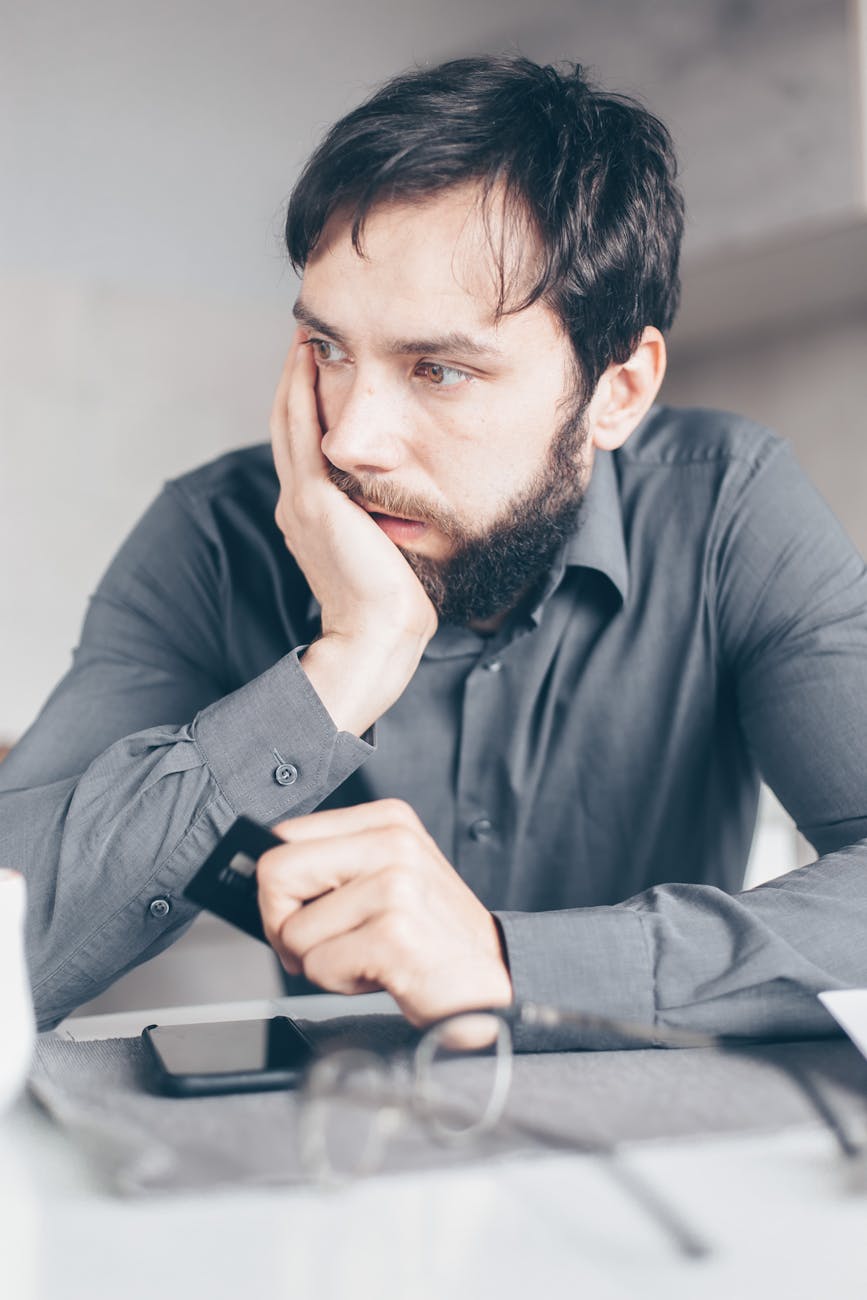 A worried man in a gray shirt holds a credit card, symbolizing online fraud or financial stress.