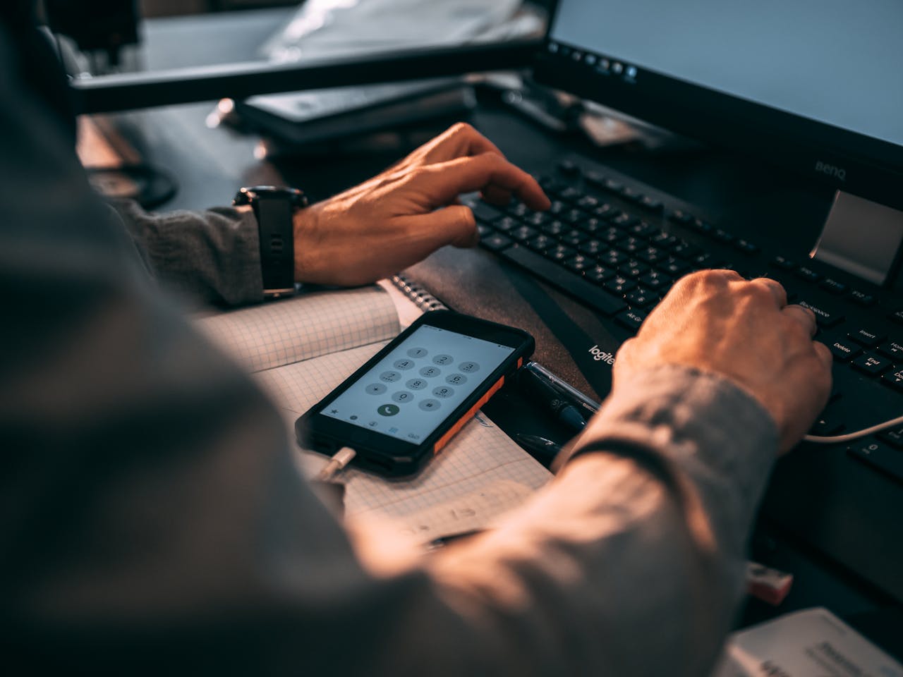 home-services-004 Businessman typing on keyboard in office with smartphone displaying numbers.