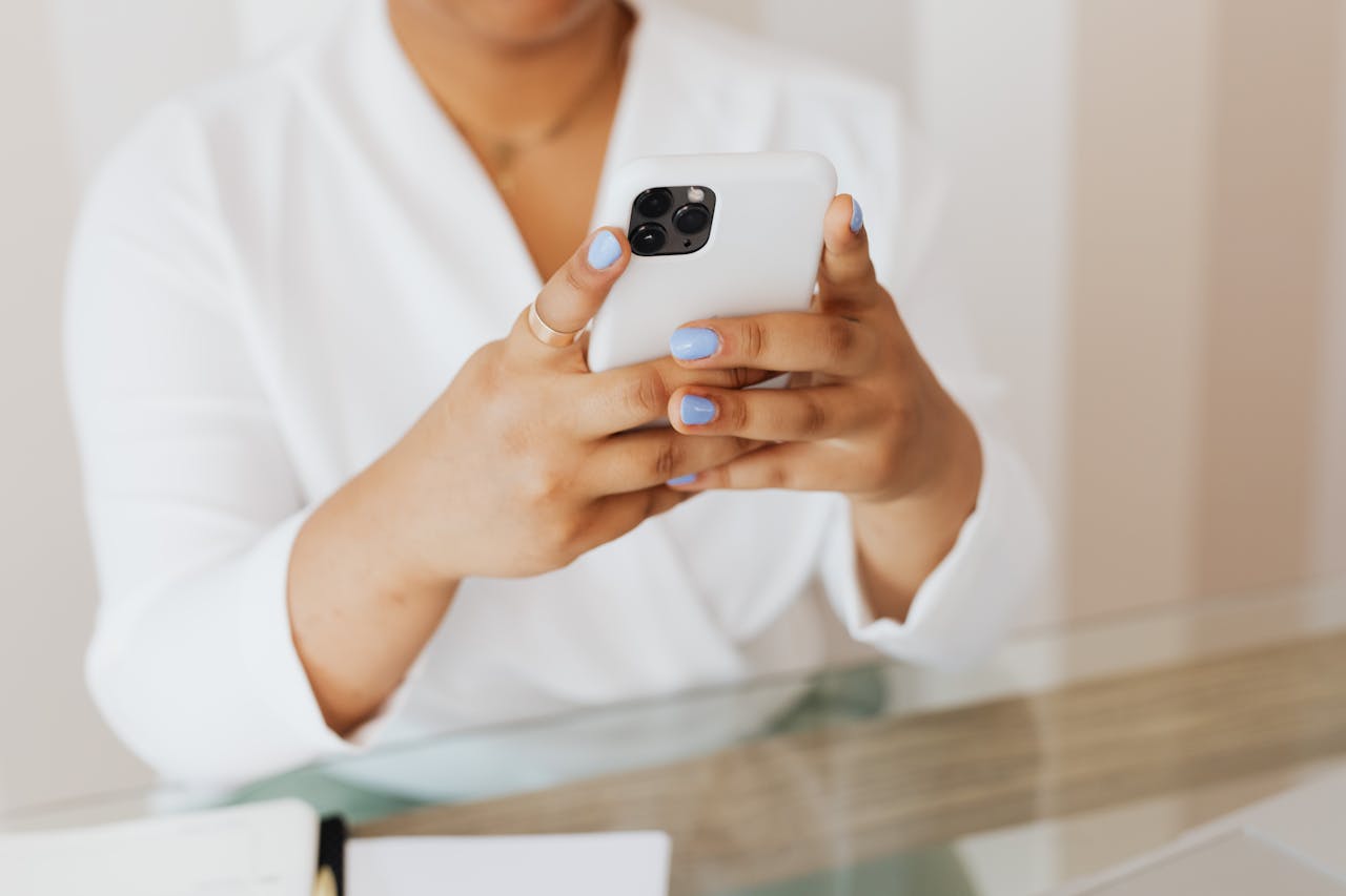 about-01 Close-up of a person holding a smartphone indoors with a focus on manicured nails.