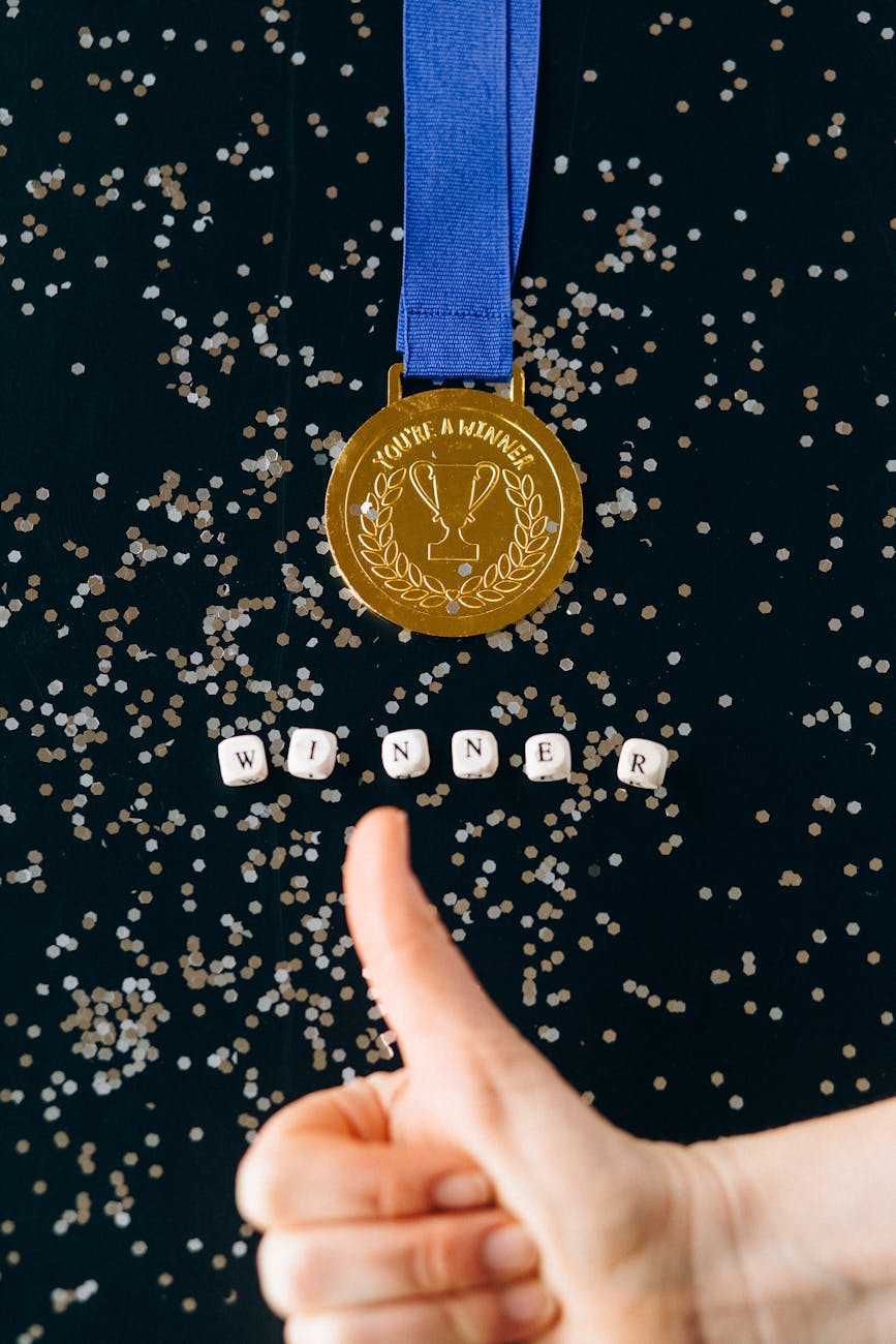 A gold medal with a thumbs up and letter blocks spelling WINNER on a dark background.